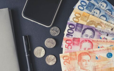 Flat lay of Philippine peso bills, coins, smartphone, and notebook. Ideal for financial themes.