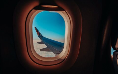 Scenic view from an airplane window showing the aircraft wing against a bright blue sky.