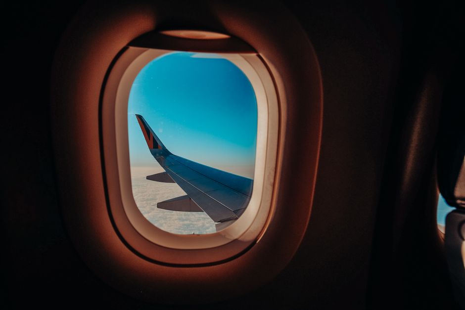 Scenic view from an airplane window showing the aircraft wing against a bright blue sky.