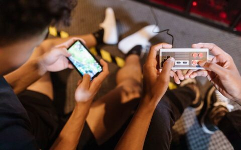 Close-up of teenagers playing mobile and retro video games indoors, showcasing fun and technology.