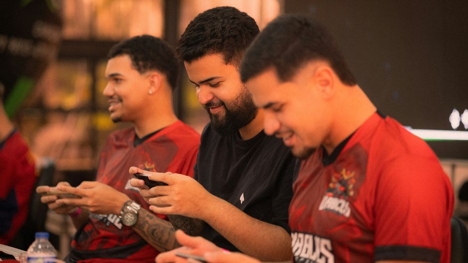 Three young men focus intensely on a mobile gaming competition indoors.