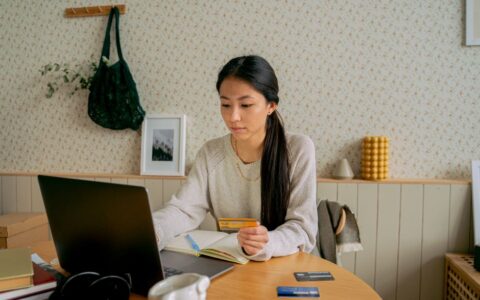 A woman using a laptop and credit card for online shopping at a cozy indoor setting.