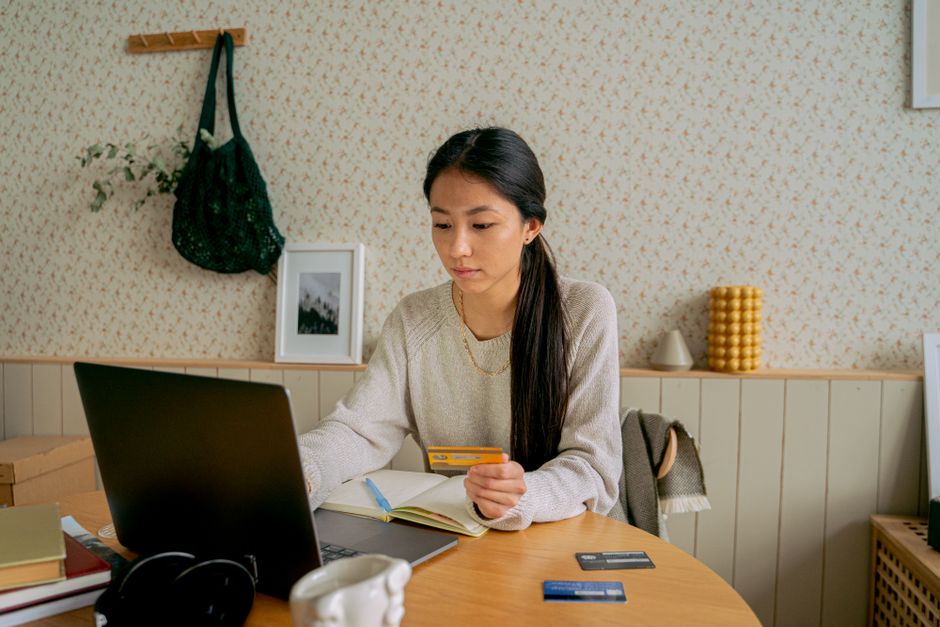 A woman using a laptop and credit card for online shopping at a cozy indoor setting.