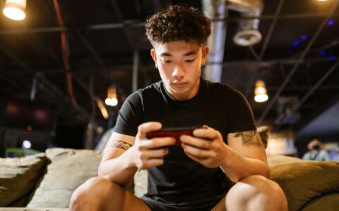 Focused young man engaged in gaming on smartphone indoors, enjoying online recreation.