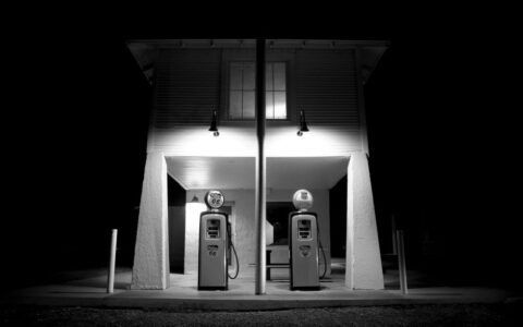 A black and white photograph of a vintage gas station illuminated at night, showcasing nostalgia.