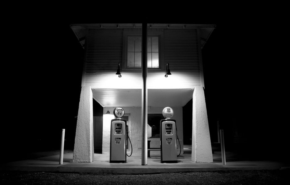 A black and white photograph of a vintage gas station illuminated at night, showcasing nostalgia.