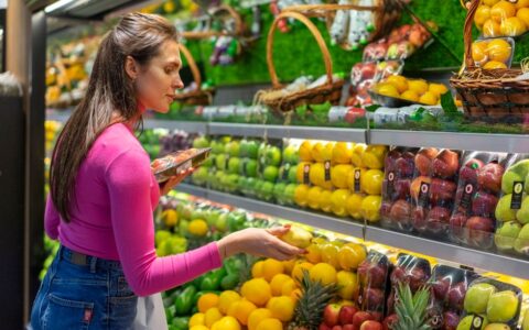 A woman examines fresh fruits in a vibrant grocery store produce section, shopping for healthy options.