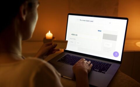 A woman makes a secure online payment using a laptop and credit card in a cozy setting.