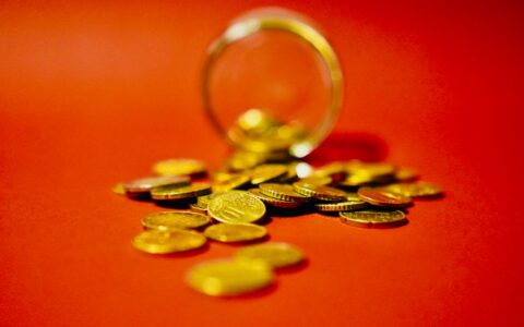 A collection of golden coins spilling from a glass jar on a vibrant red background symbolizes wealth.