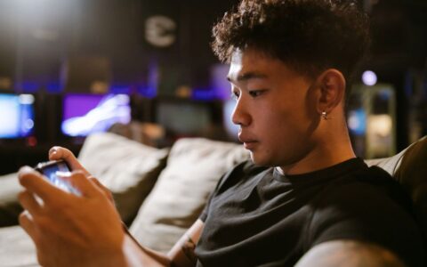 Close-up of a young Asian man immersed in mobile gaming indoors, highlighting modern technology and recreation.