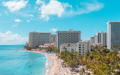 A vibrant aerial view of Waikiki Beach with luxurious hotels and sunlit turquoise ocean.