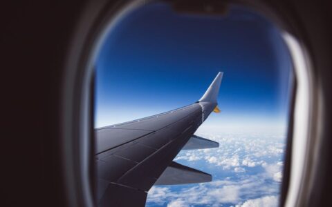 A view from an airplane window showing the wing and clouds below, captured in daylight.