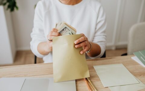 Close-up of person holding envelopes with cash at a wooden desk indoors.