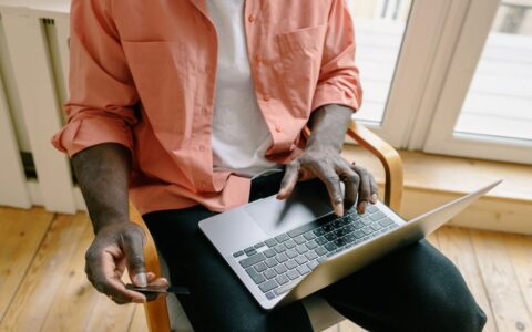 A man uses a laptop and credit card for online shopping in a home setting, reflecting modern cashless transactions.