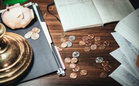 From above coins scattered on desk near financial papers and lovely pig wallet in accountant office