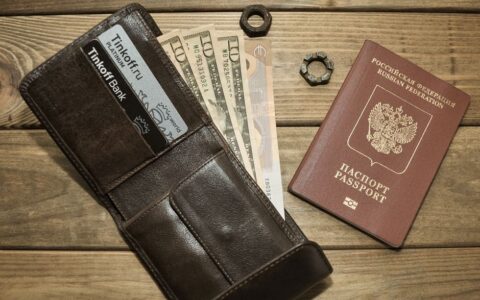Brown leather wallet with cards, assorted currencies, and passport on wood surface.