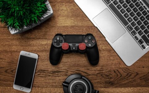 A flat lay photo showcasing a gaming console, laptop, smartphone, and headphones on a wooden tabletop.