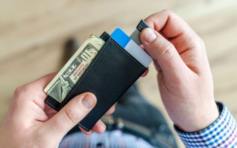 Close-up of a man's hands holding a wallet with cash and credit cards, indicating financial management.
