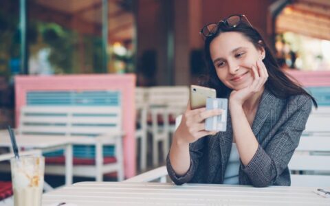 Smiling woman using smartphone and credit card at cafe for online shopping.