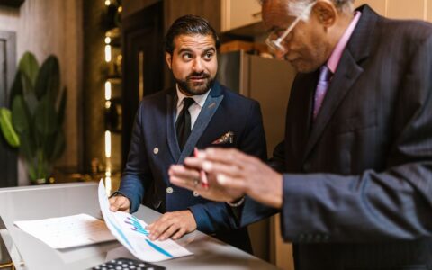 Two men in suits discuss financial documents with graphs indoors.
