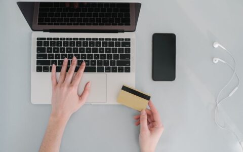 Flat lay of a workspace with a laptop, bank card, smartphone, and earphones, ideal for online finance themes.