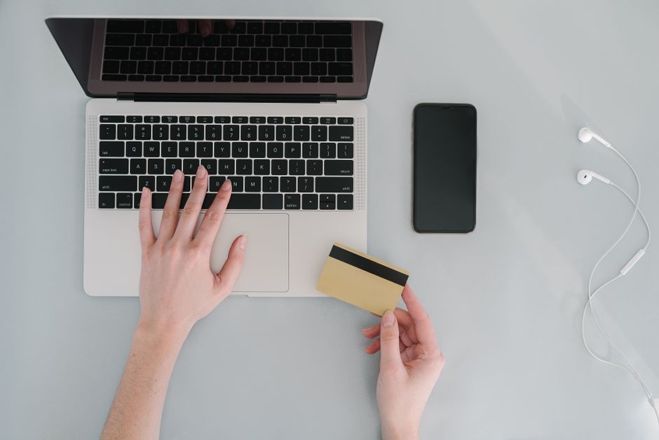 Flat lay of a workspace with a laptop, bank card, smartphone, and earphones, ideal for online finance themes.