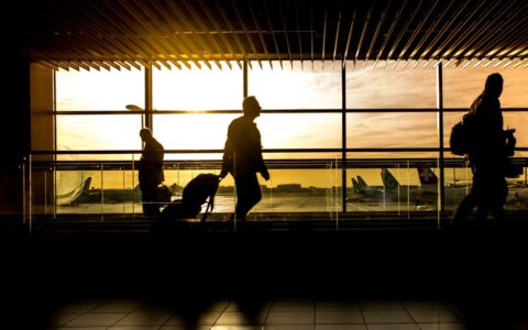 Travelers in silhouette pulling luggage at the airport during a beautiful sunset.