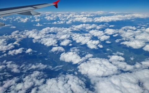 A breathtaking view of clouds and mountains from an airplane window, showcasing a serene and vast sky.