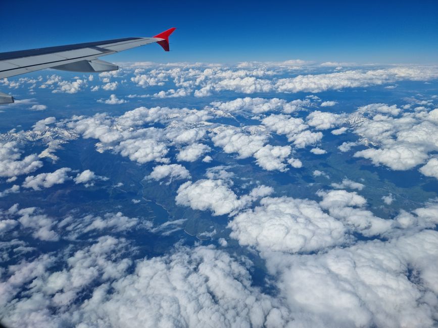 A breathtaking view of clouds and mountains from an airplane window, showcasing a serene and vast sky.
