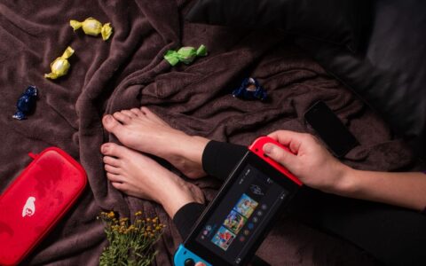 Close-up of a person playing Nintendo Switch with candy and a cozy blanket.