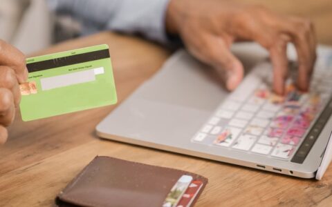 Person using a credit card for an online purchase on a laptop at a wooden table.