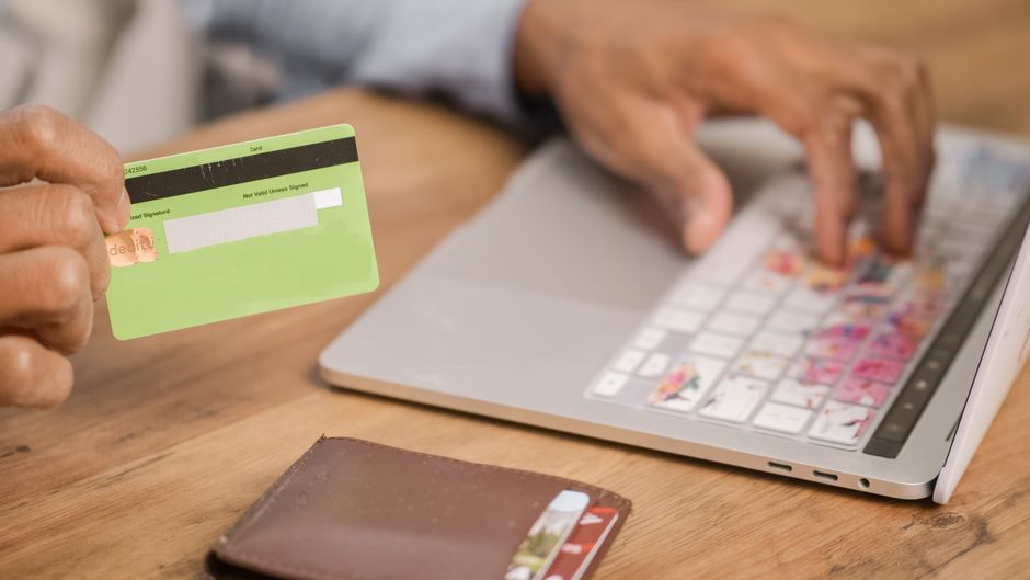 Person using a credit card for an online purchase on a laptop at a wooden table.