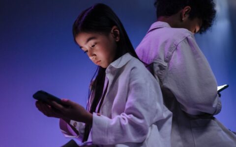Two children engrossed in using their smartphones in a dimly lit setting.