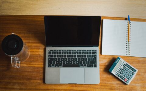 Flat lay of workspace featuring a laptop, calculator, and notebook on a wooden desk.