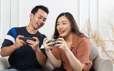 Young couple enjoying gaming on smartphones indoors, capturing joy and togetherness.
