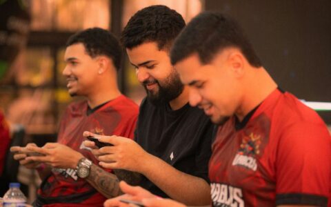 Three young men focus intensely on a mobile gaming competition indoors.